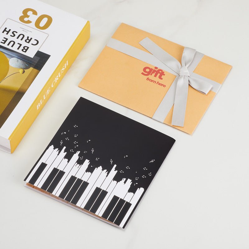 3D Pop-Up Piano Greeting Card with a black cover featuring piano keys and musical notes, alongside gift packaging