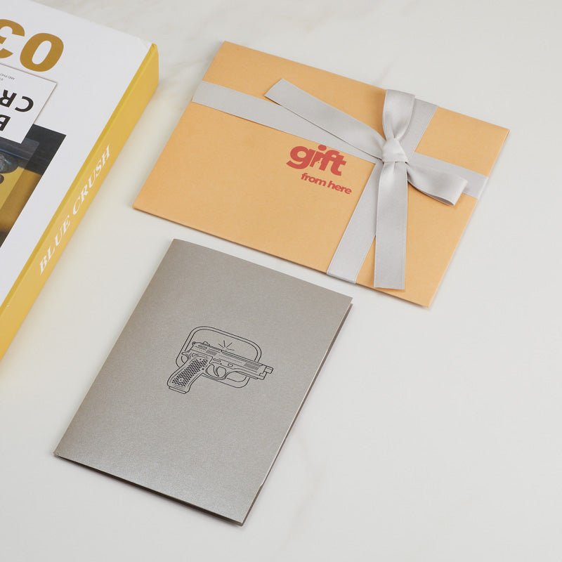 3D Pop-Up Handgun Greeting Card with a grey cover alongside gift packaging