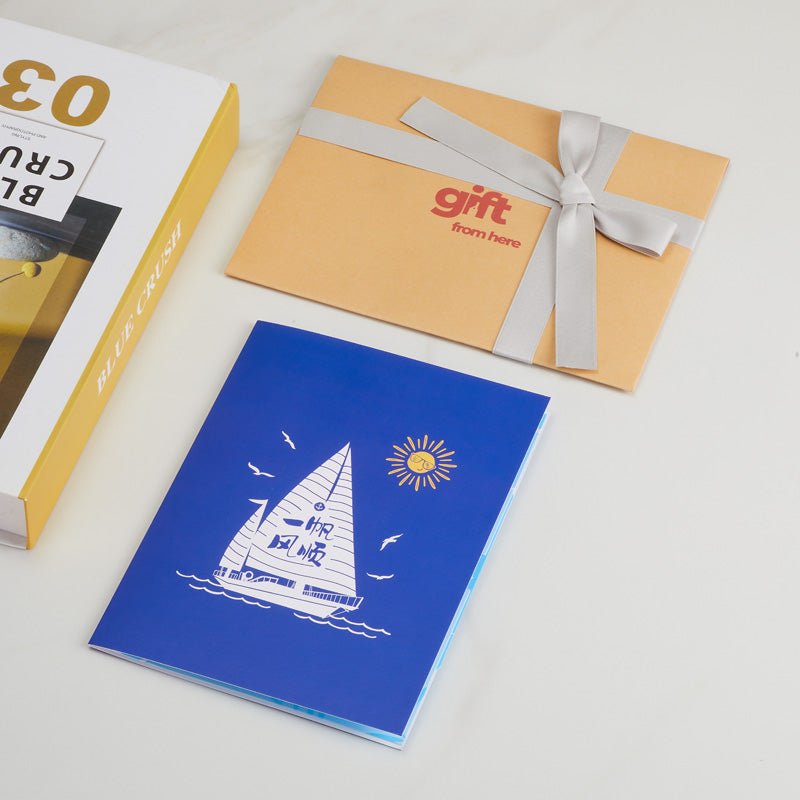 Pop-up greeting card displayed with a gift box and envelope, the cover design of a sailboat and the words "Happy Birthday."