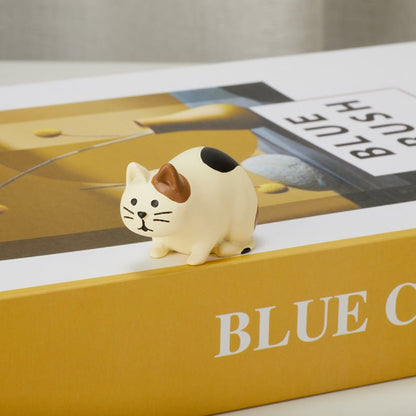 Cute crouching cat figurine on a book, side view