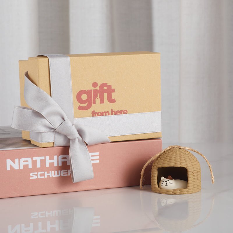 a gift box with a ribbon and a small straw hut with a sleeping cat ornament beside it.