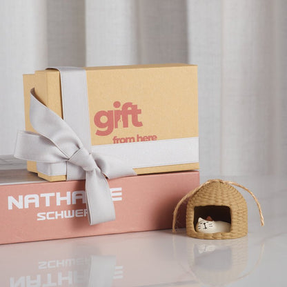 a gift box with a ribbon and a small straw hut with a sleeping cat ornament beside it.