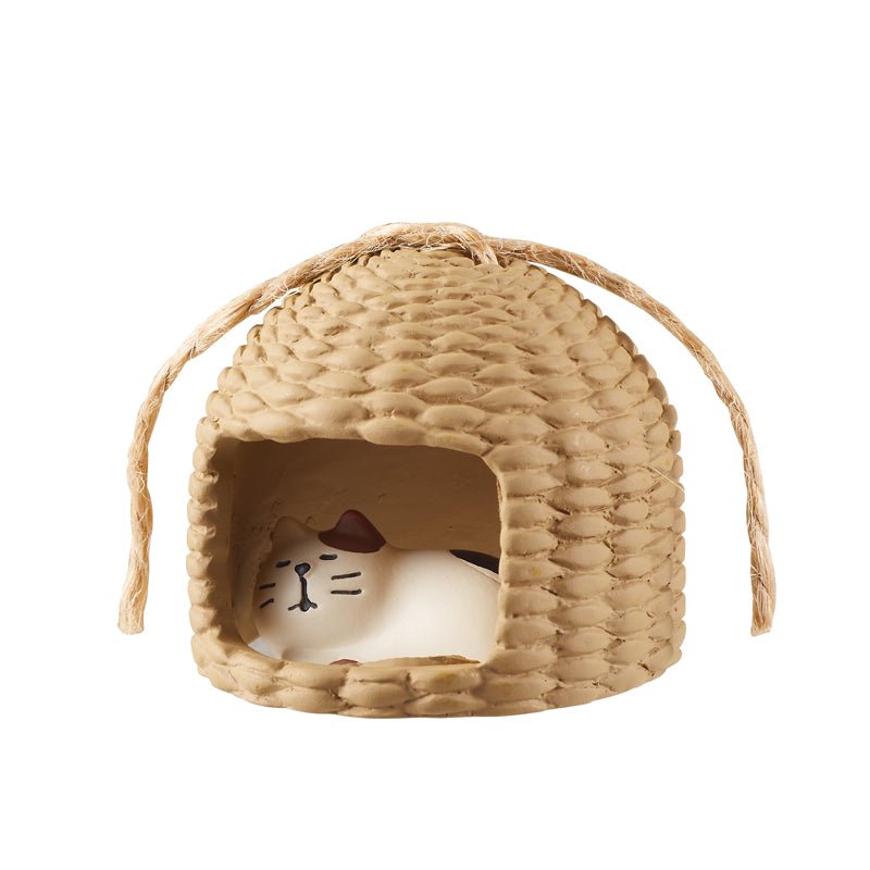 a small straw hut ornament with a sleeping cat inside.