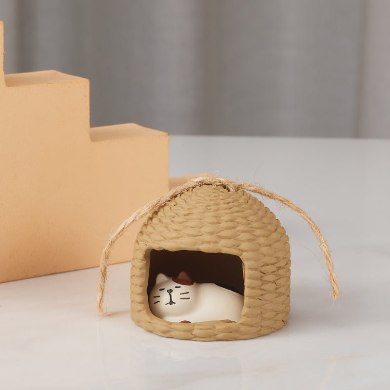 Small straw hut with a sleeping cat ornament displayed on a white table