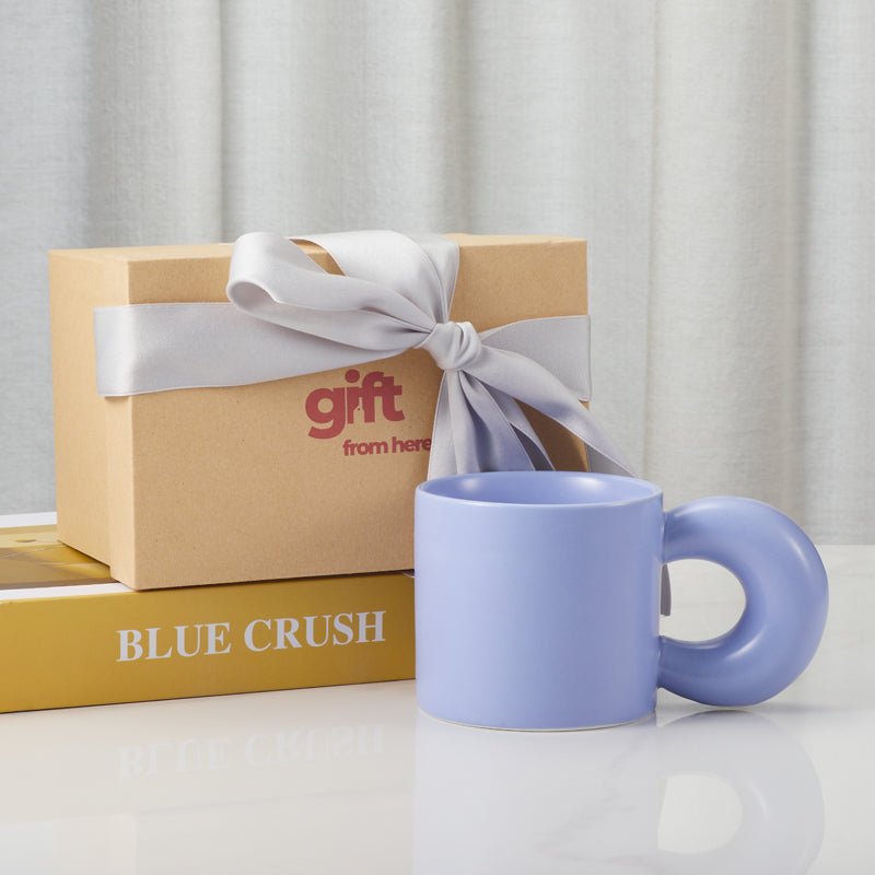 Light blue ceramic mug with a round handle next to a gift box with a ribbon