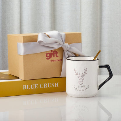 Ceramic mug with deer design and gold spoon next to a gift box