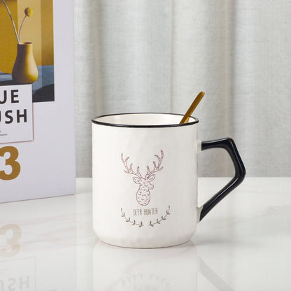 Ceramic mug with deer design and gold spoon on a table