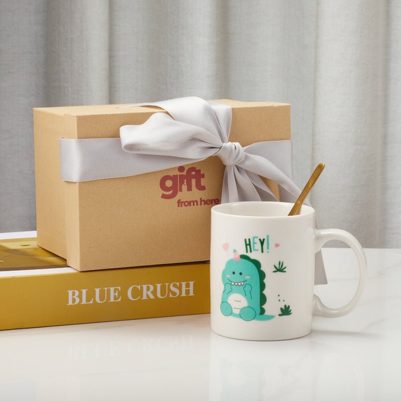 White ceramic mug with dinosaur illustration and a gift box with ribbon