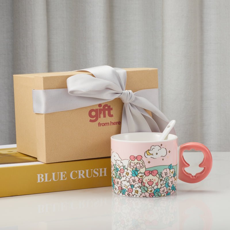 Ceramic mug with a pink floral design and a coral-colored floral-shaped handle, next to a gift box