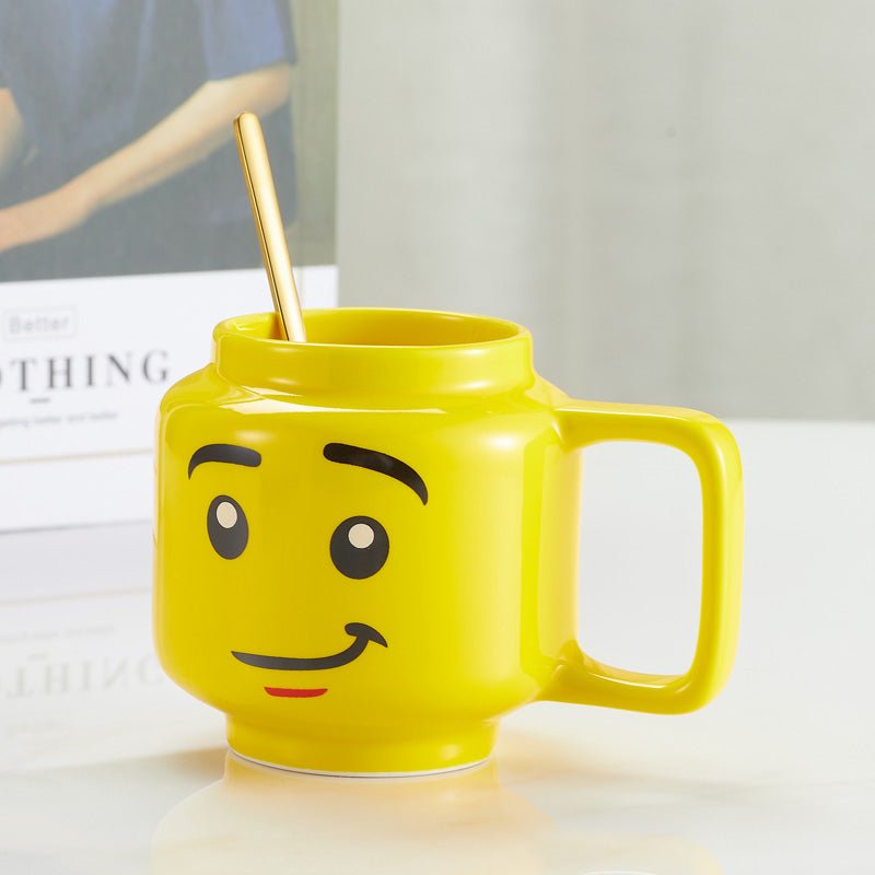 Yellow mug with a smiling face design and a golden spoon, placed on a table next to a book